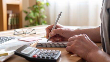 Person’s,Hands,Using,A,Calculator,And,Writing,Notes,In,A